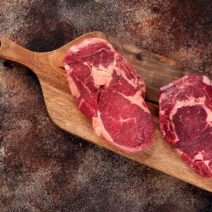 Raw ribeye steak on a wooden board, top view