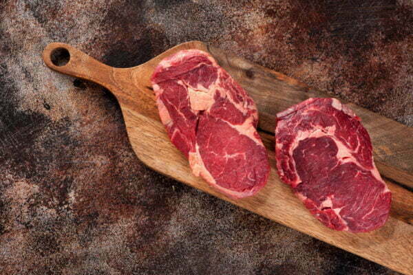 Raw ribeye steak on a wooden board, top view